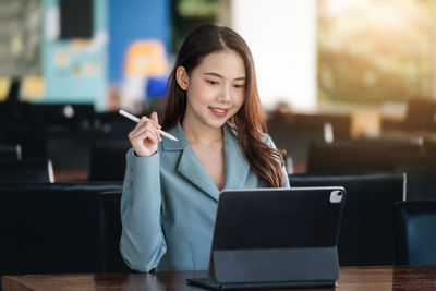 Young woman using mobile phone while sitting on table