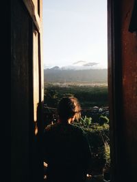 Rear view of man looking through window