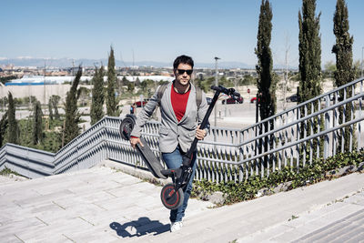 Full length of businessman holding push scooter while walking on steps outdoors