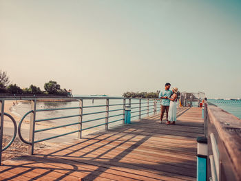 People on pier by sea against clear sky