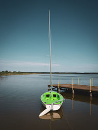 A small green sailing boat is attached to a lake at a landing stage