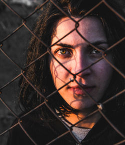 Close-up portrait of young woman against chainlink fence