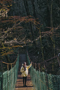 Woman standing on footbridge in forest