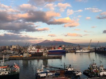 Boats moored at harbor against cloudy sky