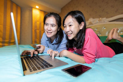 Portrait of smiling young woman using smart phone on bed