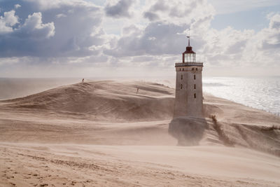 Rubjerg knude lighthouse on coast against cloudy sky