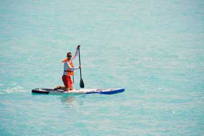 Young man dressed in swimsuit and lifevest paddling on stand up paddle board