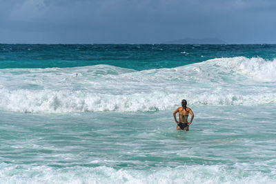 Woman standing in sea with waves on tropical beach with turquoise ocean