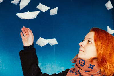 Woman looking at paper boats hanging against blue wall