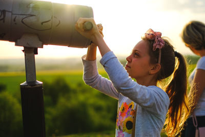 Side view of girl holding telescope during sunset