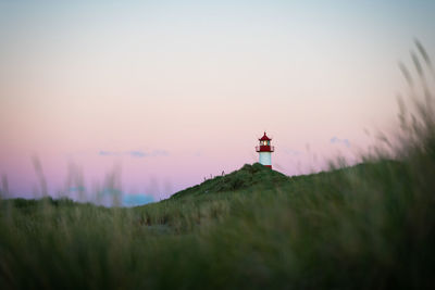 Lighthouse on field against sky during sunset