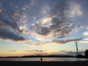 Silhouette people on shore against sky during sunset