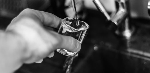 Cropped hand of person filling water in shot glass