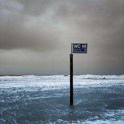 Information sign on wooden post in sea against sky