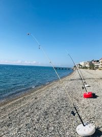 Fishing rod on beach against clear blue sky