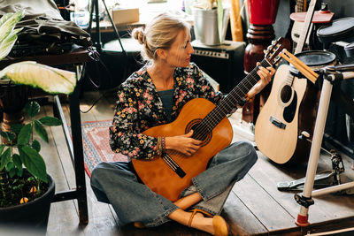 A woman plays an acoustic guitar while sitting on a stage among musical instruments.