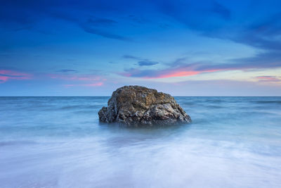 Rocks in sea against sky during sunset