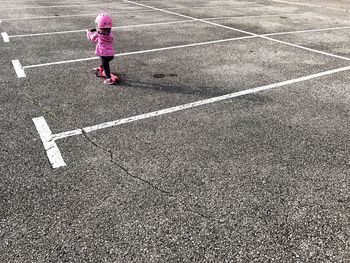 Rear view of baby girl playing with push scooter at road