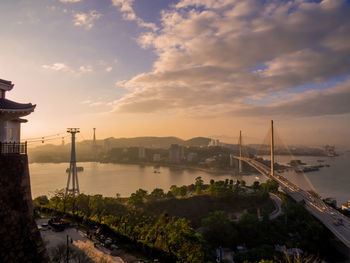 Bridge over river in city against cloudy sky