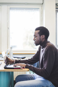 Side view of male student using laptop at table in university cafeteria