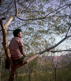 Side view of man sitting on tree in forest