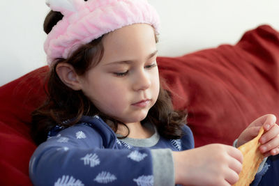 Cute little girl in a pink head dress is eating crepes on the couch