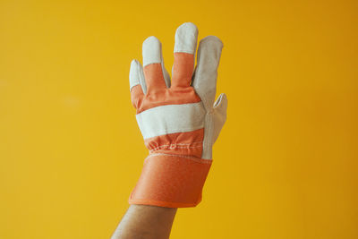 Close-up of hand wearing gloves gesturing against yellow background