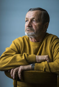 Senior man looking away while sitting on chair against blue background