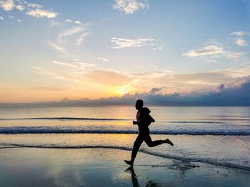 Silhouette man on beach against sky during sunset