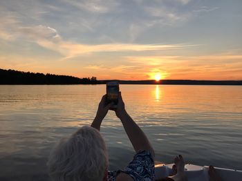 Low section of people photographing lake against sky during sunset