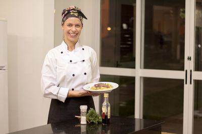 Portrait of happy female chef holding food in plate while standing in commercial kitchen
