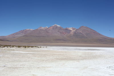 Scenic view of salt desert with mountains in background against blue sky
