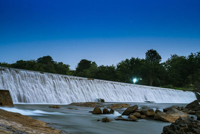 Scenic view of waterfall against clear blue sky