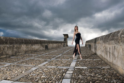 Full length of young woman on walkway against cloudy sky