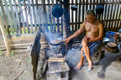 Full length of senior man cooking while sitting on chair