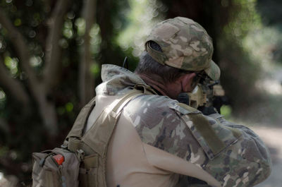 Rear view of soldier aiming with gun at forest