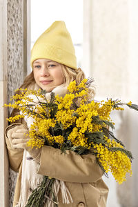  a girl in a beige coat with a bouquet of mimosa in her hands in the park.international women's day 