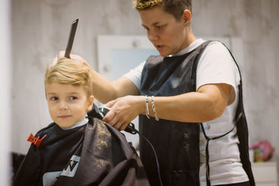 Female hairdresser styling boy hair in salon