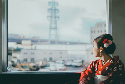 Woman wearing kimono looking through window at home