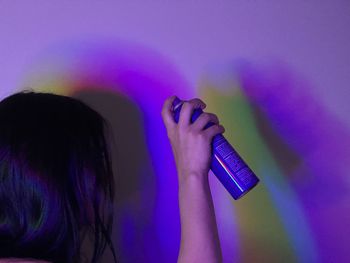Close-up of woman holding hairspray bottle against wall with colorful shadows 