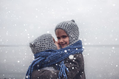 Girl in knitted grey hat hugging her frozen smaller brother