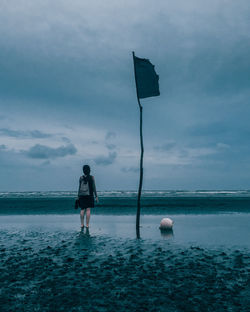 Rear view of woman standing on beach against sky