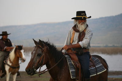 Senior man looking away riding horse against sky