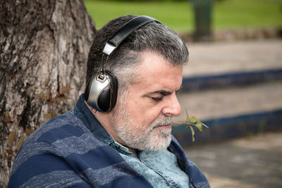 Close-up of man wearing headphones sitting by tree trunk