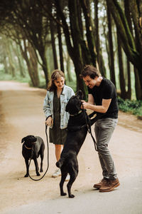 Young couple playing with two dogs on a forest road