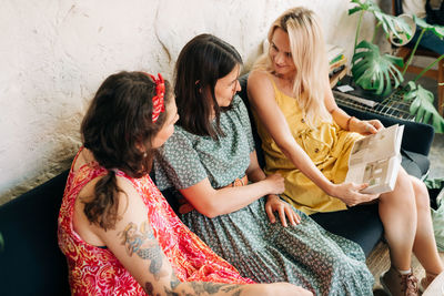 Three cheerful women friends sitting in a cafe looking at a book or album and talking.