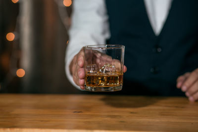 Midsection of person holding wine glass on table