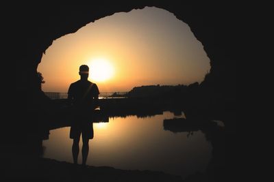 Silhouette man standing by lake against sky during sunset