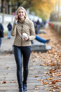 Portrait of smiling young woman talking over smart phone while walking on footpath