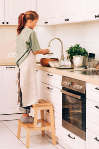 Side view of young woman standing in kitchen
